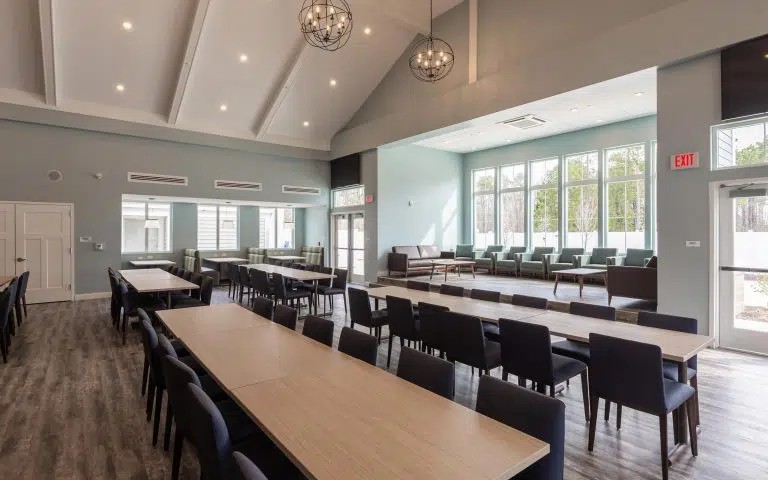 Interior dining and assembly space with long tables, chairs, high ceilings with skylights, and multiple seating areas