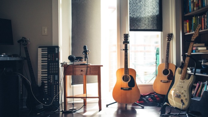 Interior creative space with multiple acoustic guitars, keyboards, microphones, recording equipment, and natural lighting from windows