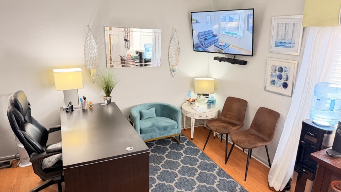 Interior office with desk, office chair, conversation seating including turquoise armchair and brown chairs, television mounted on wall
