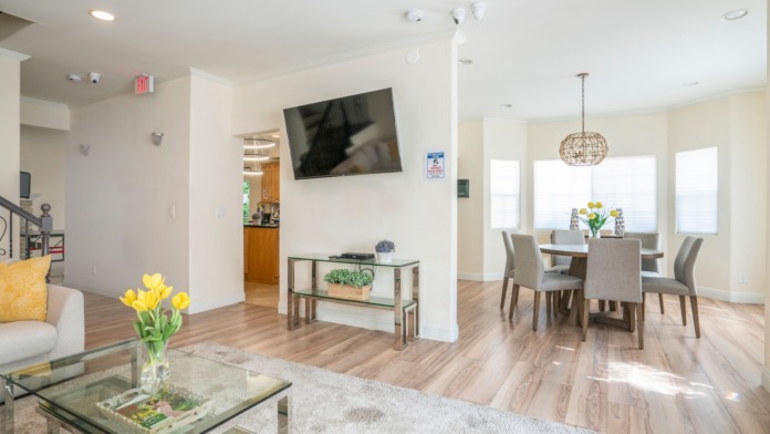 Interior living and dining area with wooden floors, glass tables, white walls, and abundant natural lighting from windows