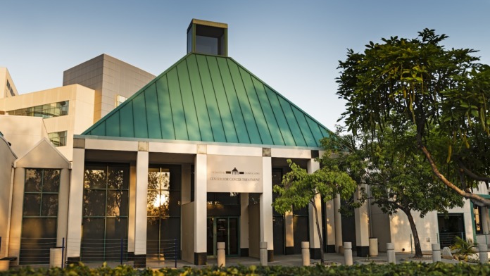 Exterior pavilion with green metal roof, white support columns, landscaping and trees creating facility entrance area