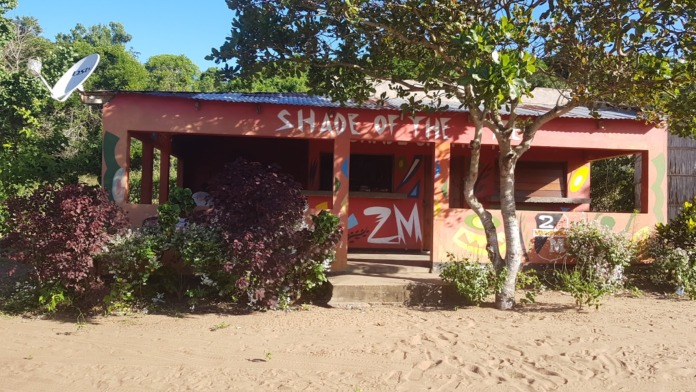 Exterior view of red-painted building with Shade of the Tree signage, surrounded by landscaping and trees