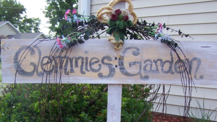 Exterior garden sign with decorative floral arrangement mounted on post, residential building and landscaping visible in background