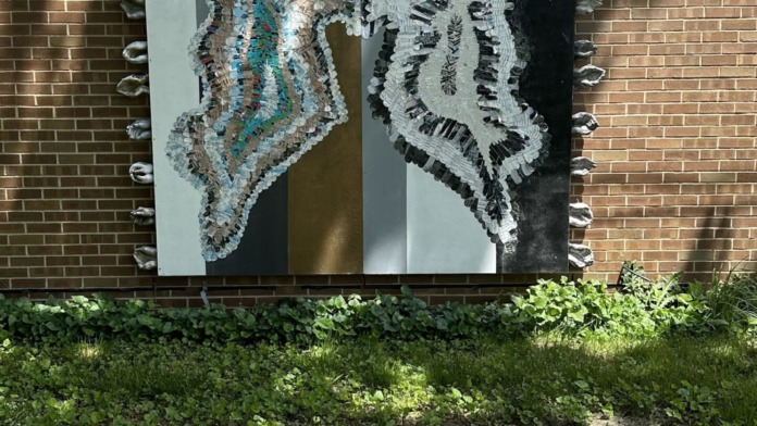 Exterior patio area featuring textured butterfly wing mural art mounted on brick building wall with landscaping