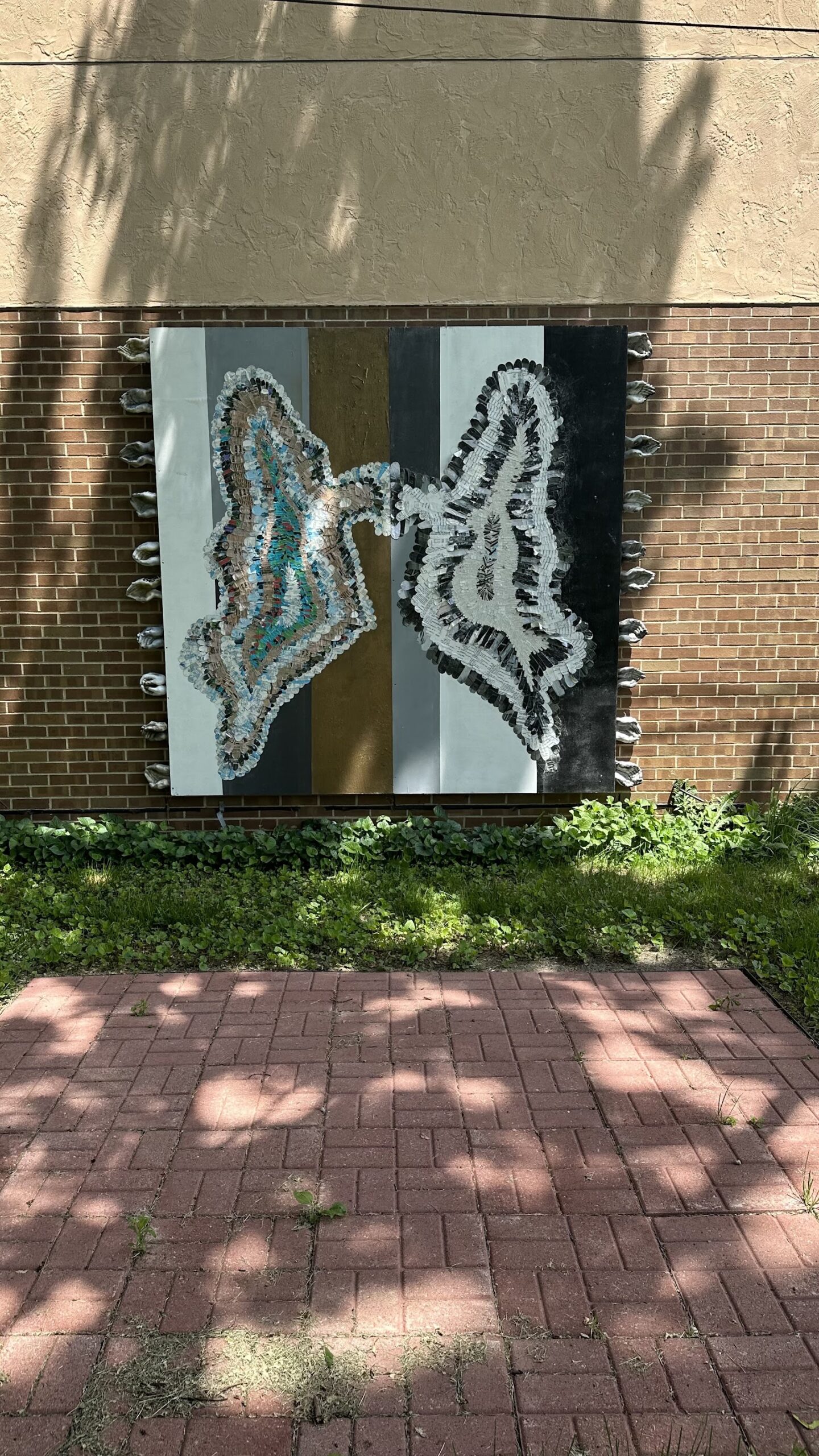 Exterior patio area featuring textured butterfly wing mural art mounted on brick building wall with landscaping