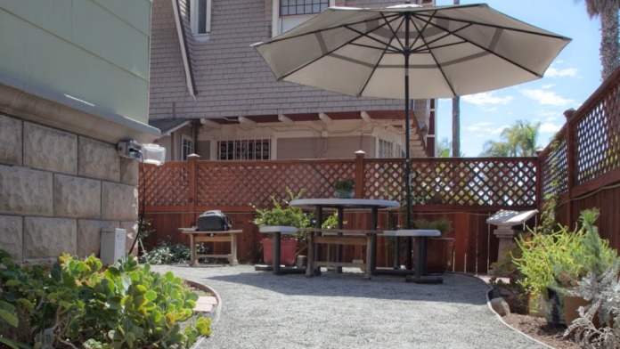 Exterior patio space with dining table, large umbrella, stone walls, wooden lattice fence, and native plantings