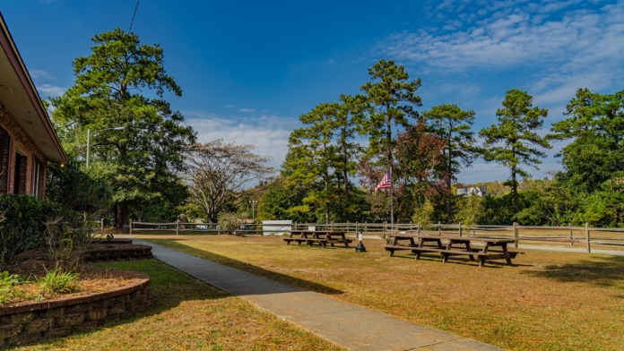 Exterior outdoor gathering space with multiple picnic tables, American flag, tree-lined grounds, and walking paths