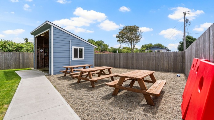 Outdoor fenced yard with picnic tables, shelter building, green lawn, and recreational games