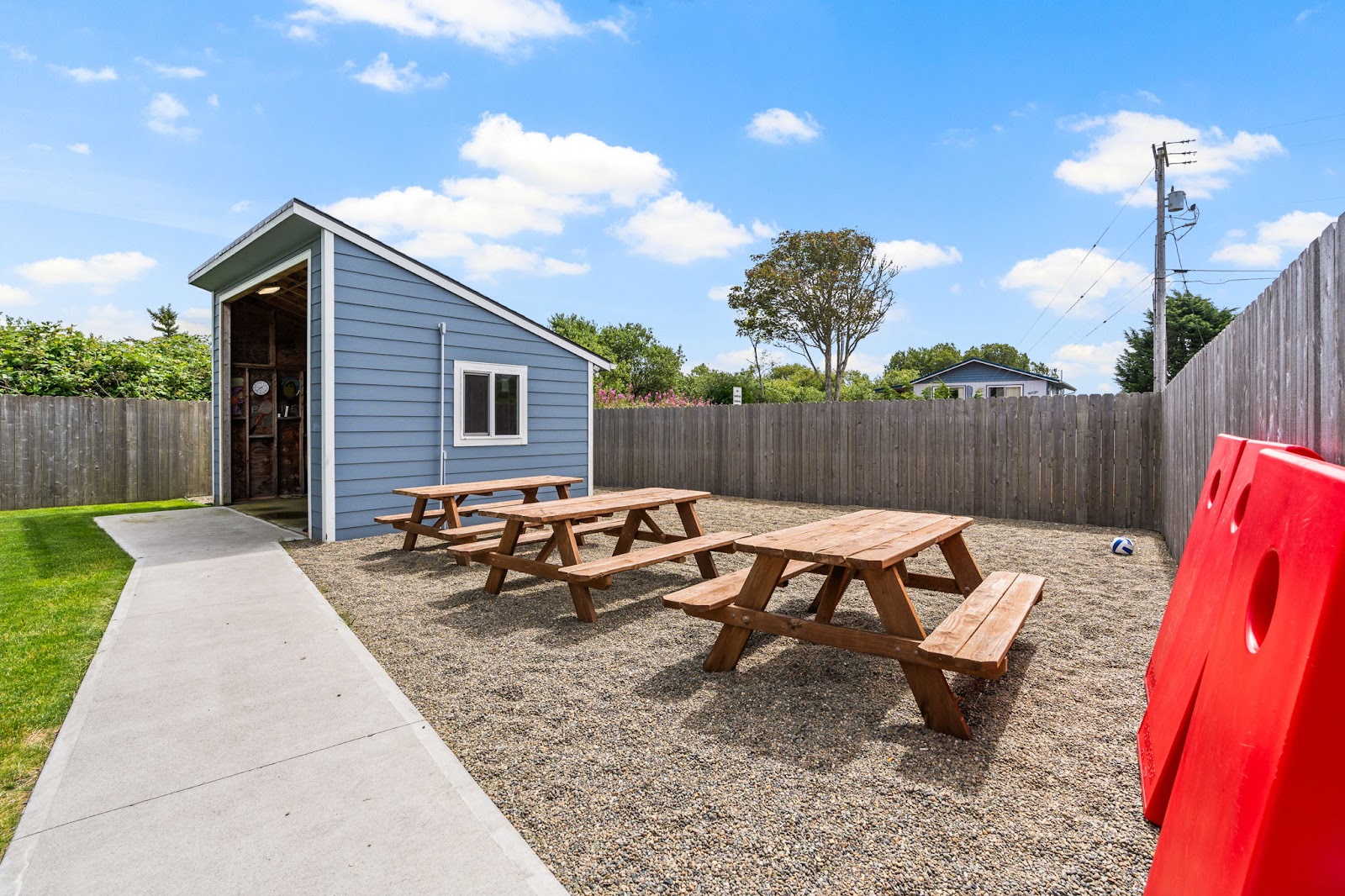 Outdoor fenced yard with picnic tables, shelter building, green lawn, and recreational games