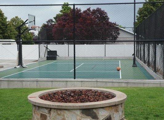 Exterior outdoor space featuring stone fire pit, sports court with basketball hoop, and manicured lawn area