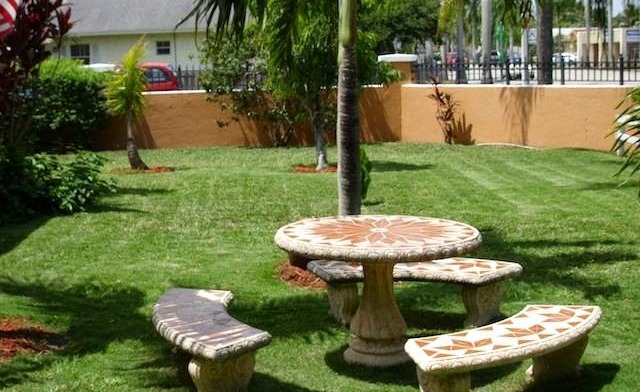 Exterior grounds showing manicured lawn, palm trees, decorative picnic table with seating, and perimeter fencing