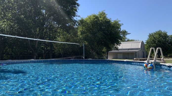 Exterior recreational pool with volleyball net, shade umbrellas, lounge chairs and landscaped grounds