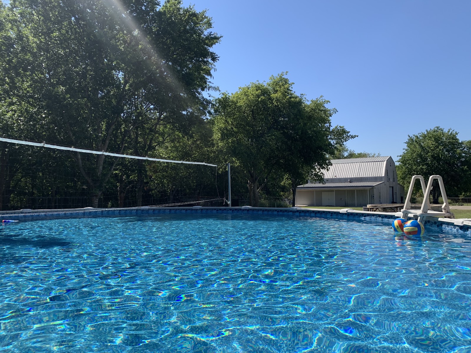 Exterior recreational pool with volleyball net, shade umbrellas, lounge chairs and landscaped grounds
