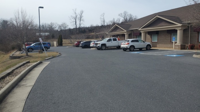 Exterior parking lot with multiple vehicles, brick building facade with gabled roof, landscaping, and accessibility parking