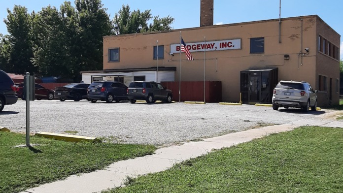 Exterior facility view showing parking lot with multiple vehicles, brick building facade, flagpole, and surrounding grounds