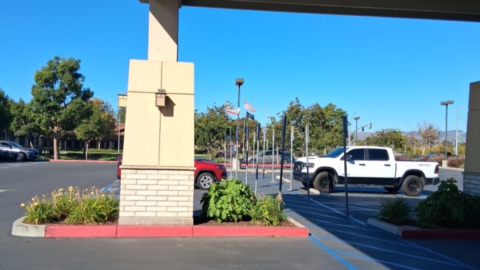 Exterior parking lot showing vehicle parking spaces, landscaping with shrubs and trees, and facility building exterior