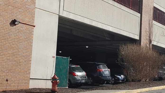 Exterior parking garage entrance with multiple vehicles visible, brick building facade, and retaining wall