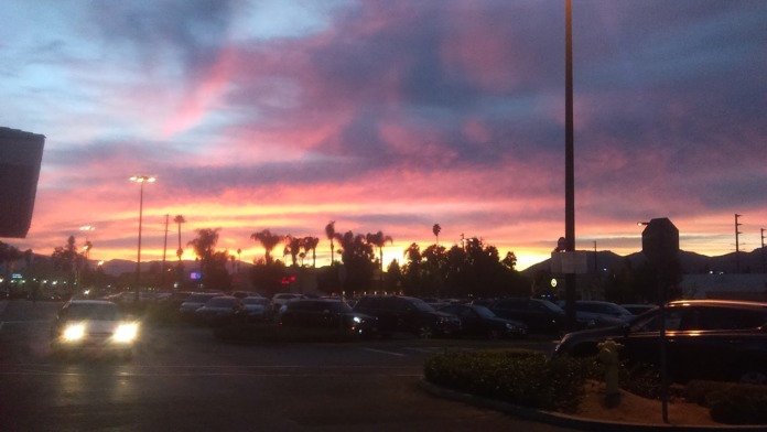 Exterior parking lot at dusk showing vehicles and facility building with dramatic sunset sky and palm trees