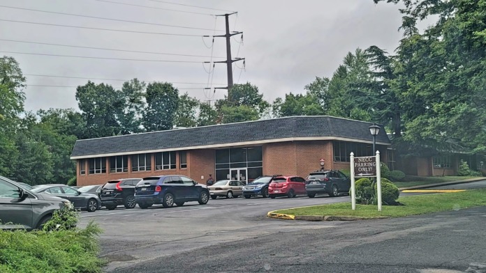 Exterior parking area with multiple vehicles, brick building entrance, and directional signage for facility access