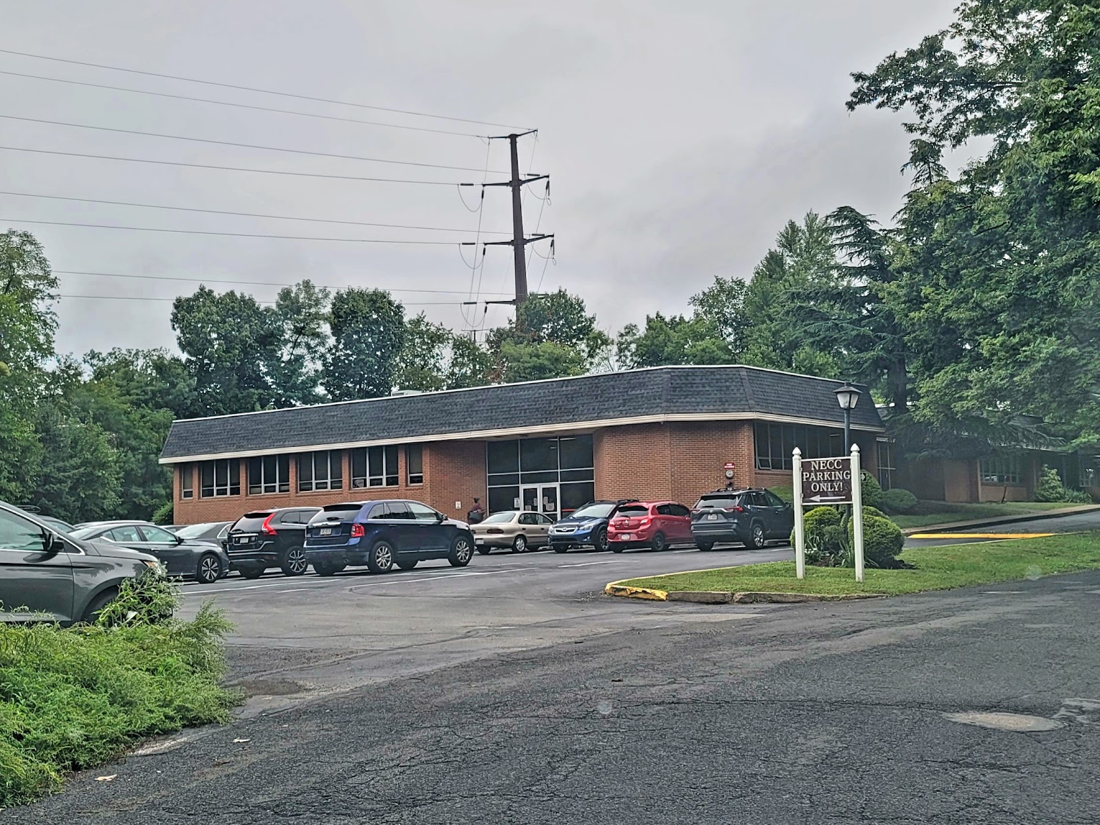 Exterior parking area with multiple vehicles, brick building entrance, and directional signage for facility access