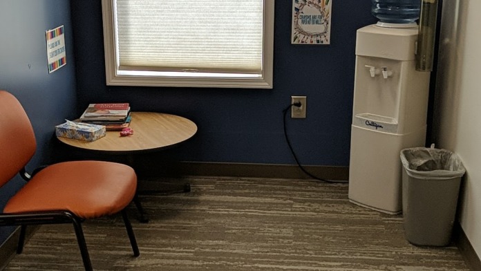 Interior activity room with dark blue walls, decorated with artwork, window, chair seating, and water cooler