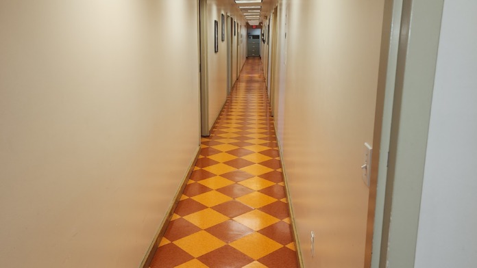 Interior residential hallway with multiple patient bedroom doors, recessed ceiling lights, and diamond patterned flooring