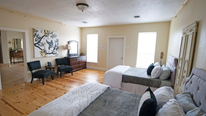 Interior patient bedroom with two beds, seating area, dresser, window with natural lighting, and decorative wall art