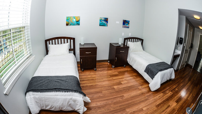 Interior residential bedroom with two twin beds, dark wood furniture, colorful wall art, natural window light, and hardwood flooring
