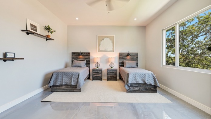 Interior bedroom with two twin beds, blue bedding, shared nightstand, lamps, wall art, and windows with nature views.