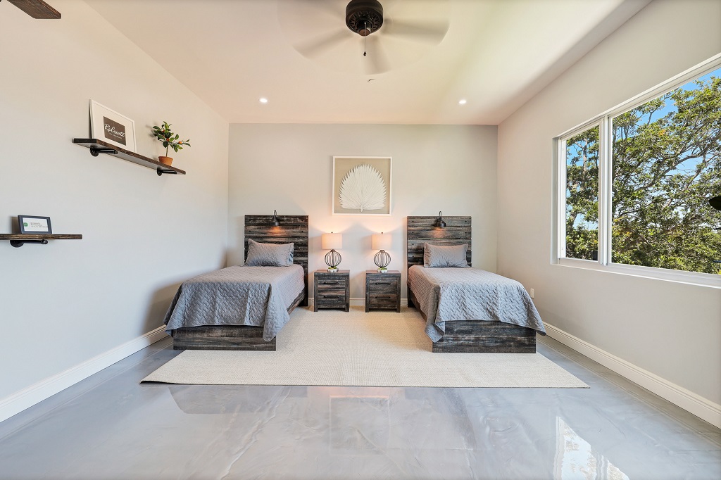 Interior bedroom with two twin beds, blue bedding, shared nightstand, lamps, wall art, and windows with nature views.
