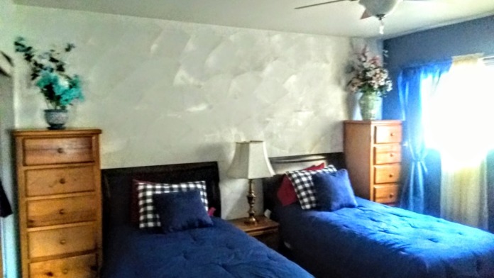 Interior patient bedroom with two double beds, striped white bedding, blue accent walls, wooden nightstands, and wall sconces