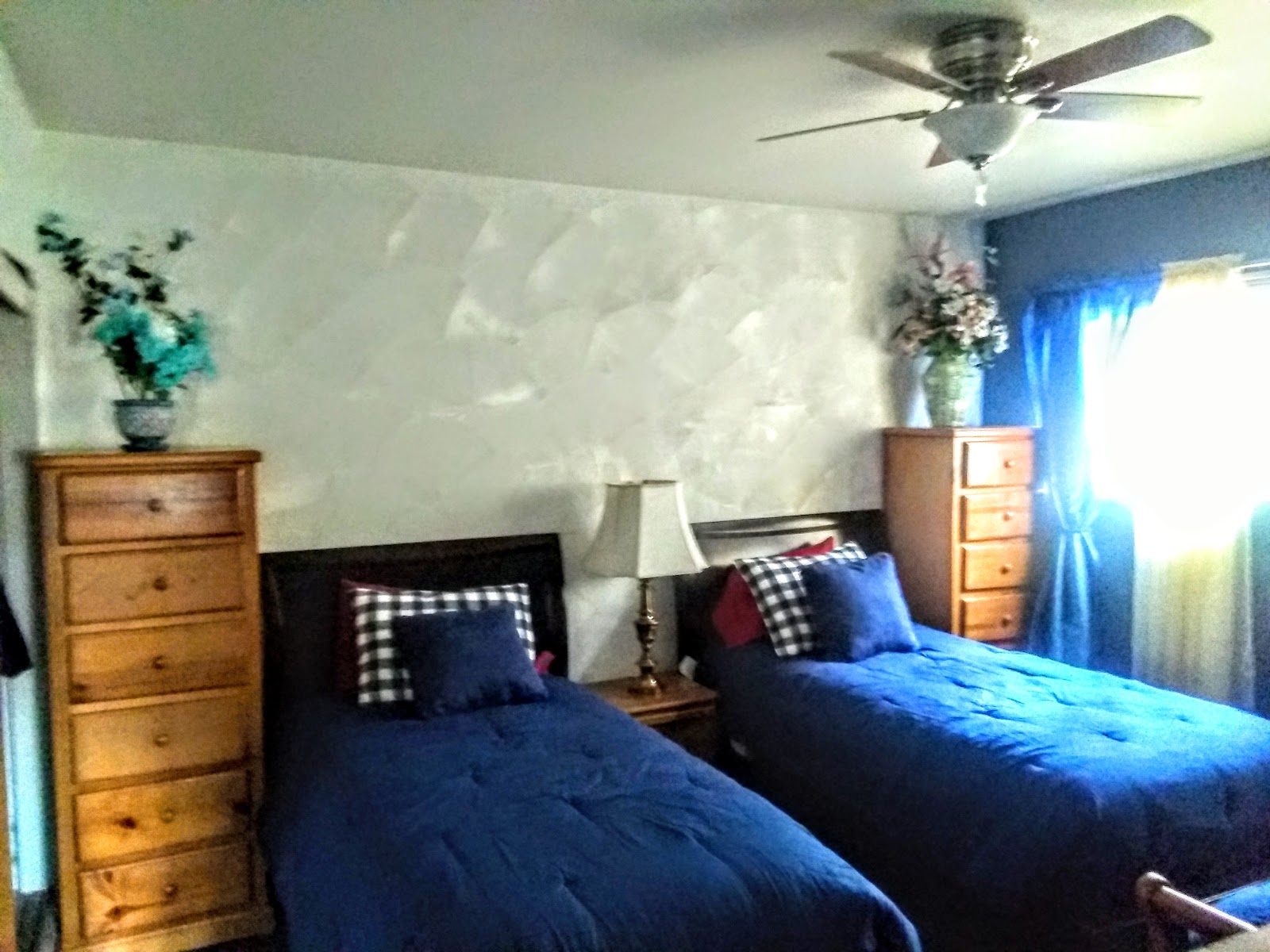 Interior patient bedroom with two double beds, striped white bedding, blue accent walls, wooden nightstands, and wall sconces