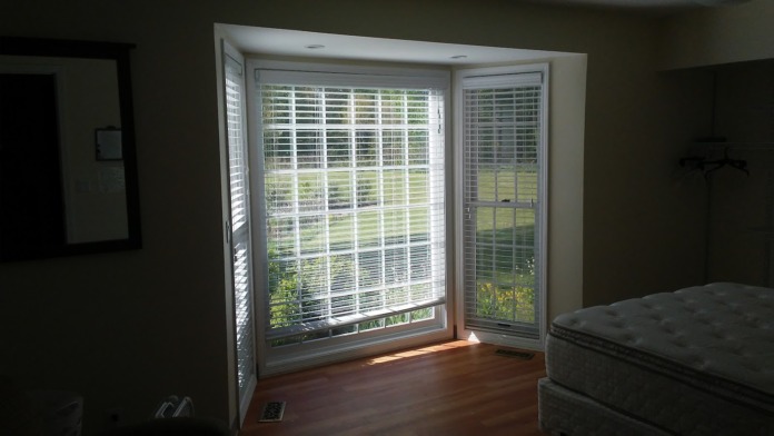 Interior patient bedroom with glass sliding doors, white shutters, hardwood flooring, and natural light from patio doors
