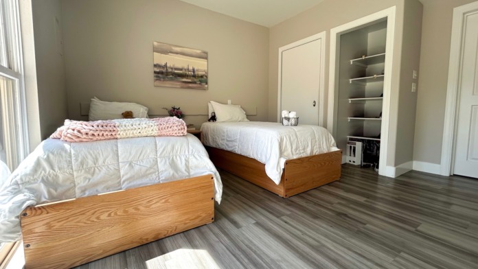 Interior patient bedroom featuring two wooden twin beds, natural lighting, artwork, and storage shelving
