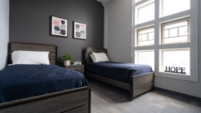 Interior bedroom with two twin beds, dark accent wall, large windows providing natural light, and modern furnishings