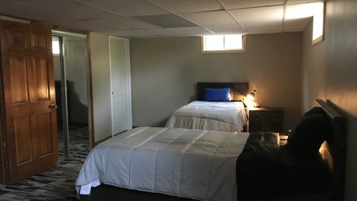 Interior patient bedroom featuring two twin beds with white bedding, wooden doors, nightstand, and natural window lighting