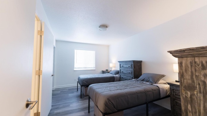 Interior bedroom with two twin beds, wood dresser, window with natural light, and hardwood flooring