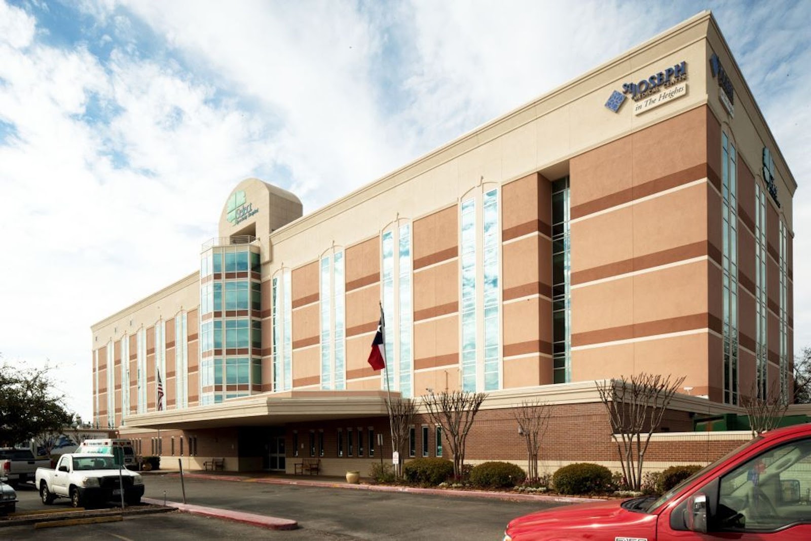 Exterior of medical facility building with tan and brick construction, large windows, landscaped entry area with flags