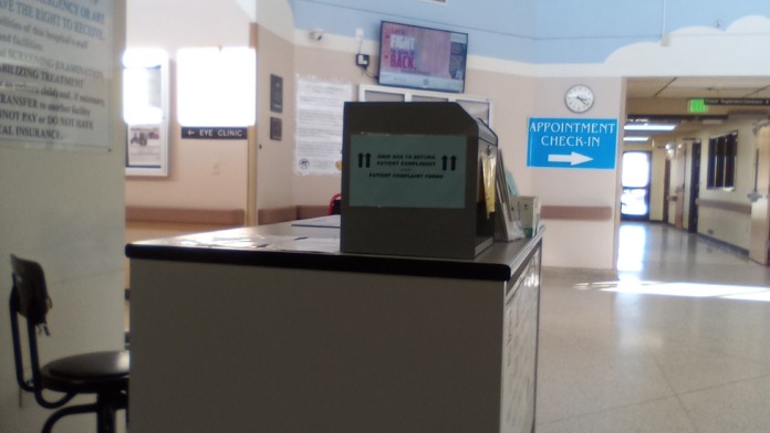 Interior waiting room with check-in desk featuring electronic display, appointment signage, and patient seating