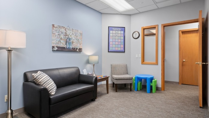 Interior room with black sofa, upholstered seating, wooden shelving, blue walls, framed artwork, and colored accent elements