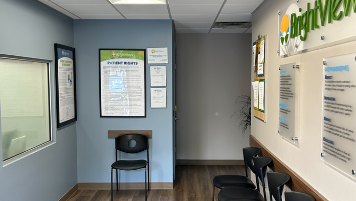 Interior reception area with blue walls, black chairs, informational posters, and patient rights signage displayed.