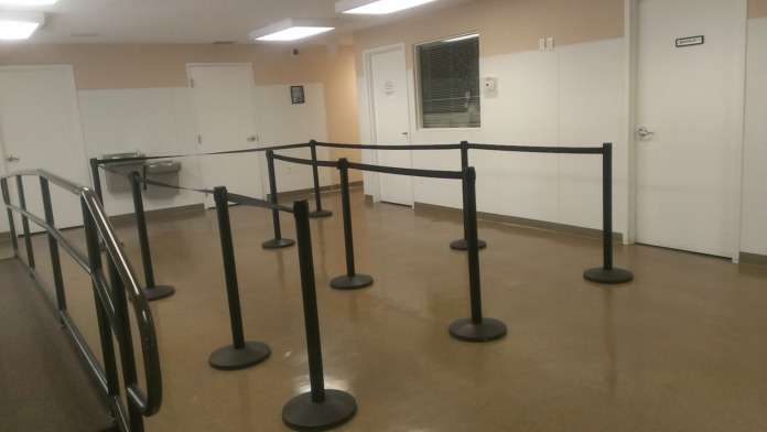 Interior hallway with organized queue barriers, white doors, and beige walls with overhead lighting