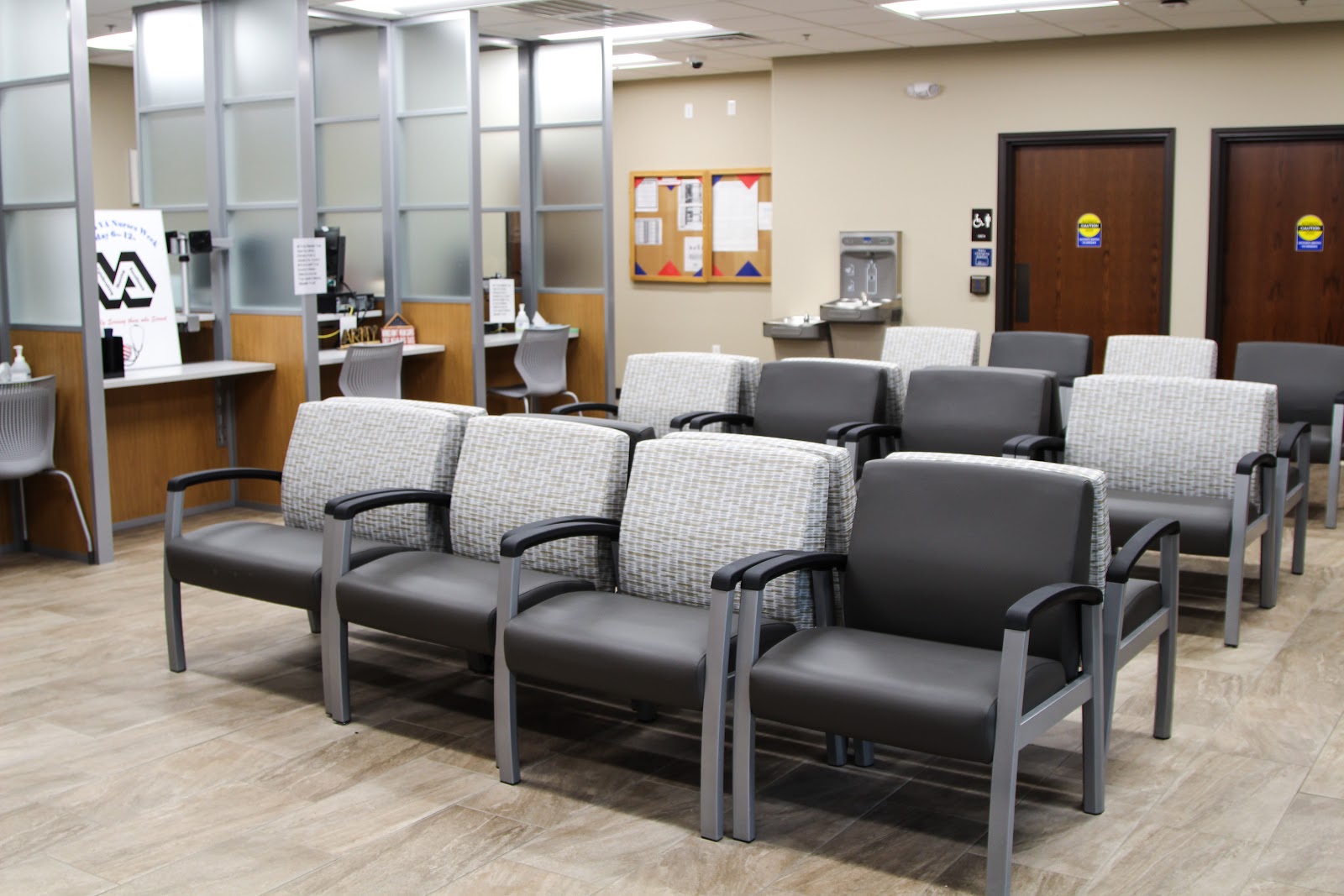 Interior waiting room with multiple upholstered chairs, reception desk with glass partitions, and water station