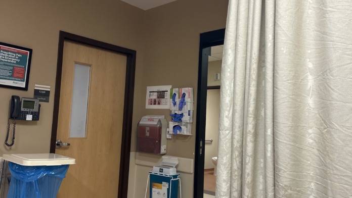 Interior hallway with wooden doors, beige walls, mounted phone, signage, blue waste receptacle, and fabric privacy curtain in doorway entrance