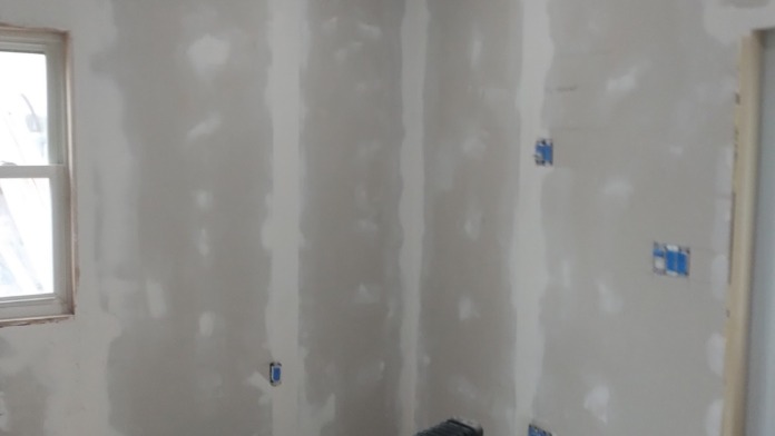 Interior patient room in renovation phase with exposed drywall, windows with protective tape, and heating equipment