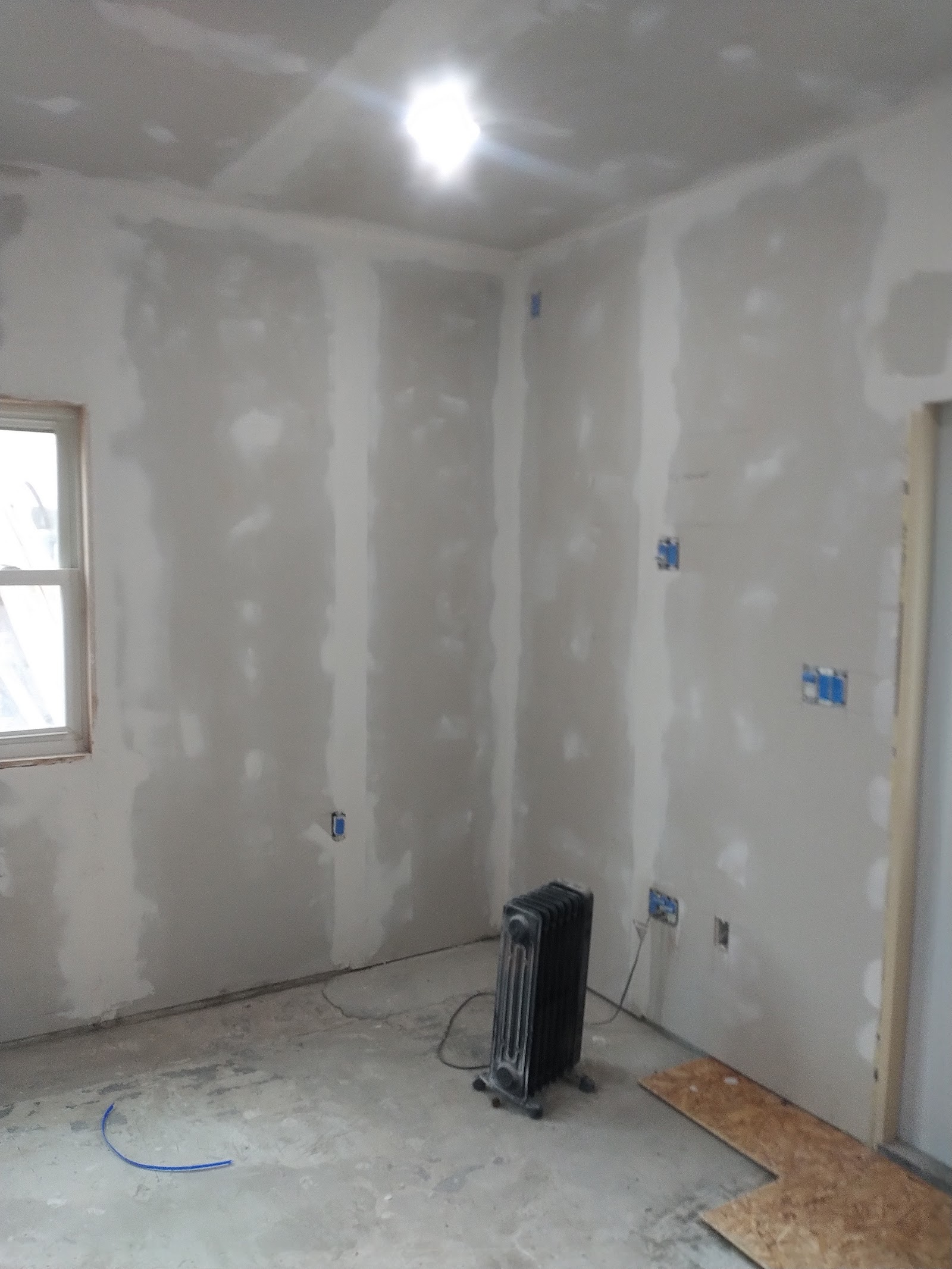 Interior patient room in renovation phase with exposed drywall, windows with protective tape, and heating equipment
