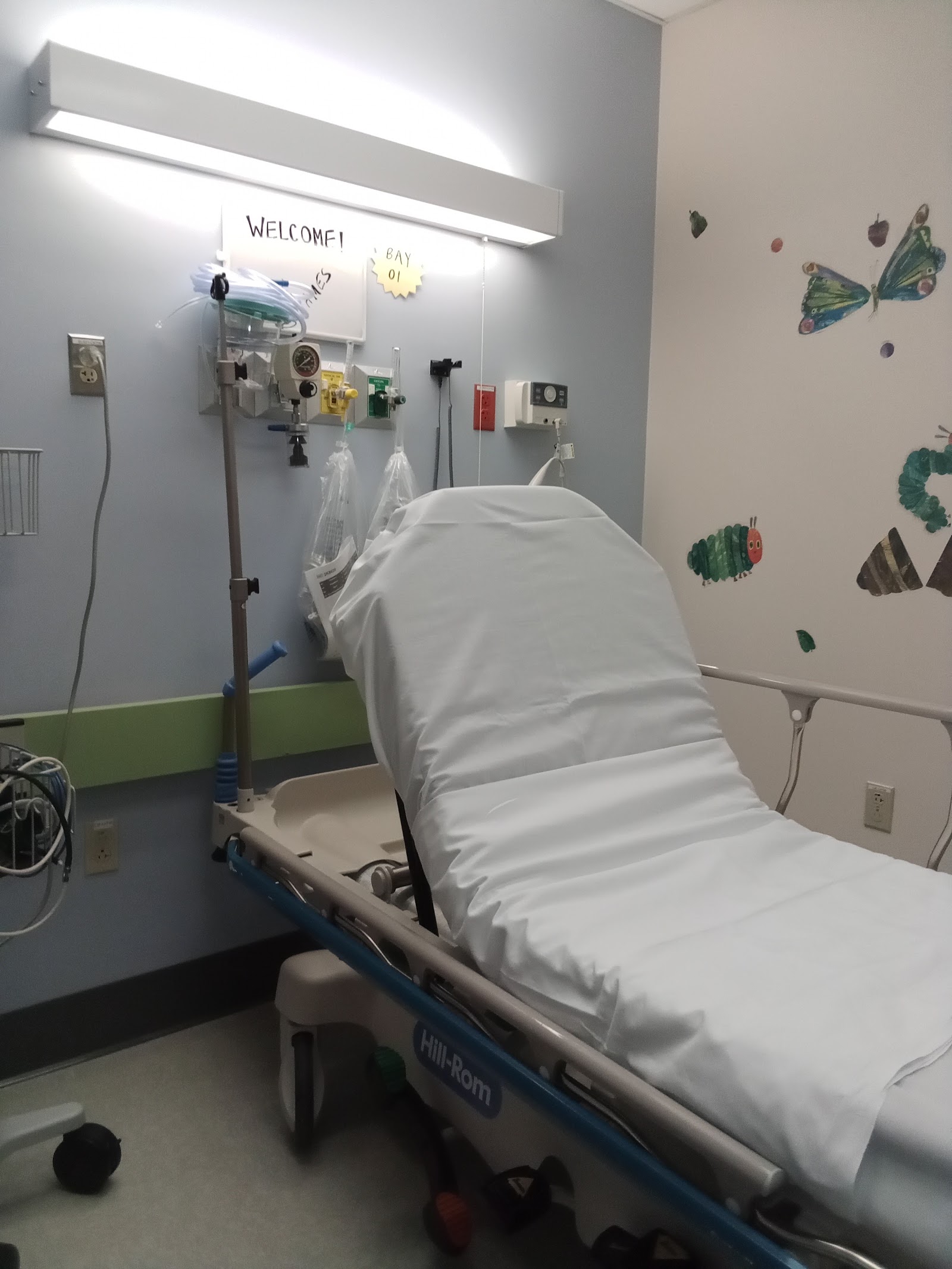 Interior patient treatment room with medical bed, equipment, monitoring devices, and child-friendly wall art