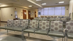 Interior community lounge with multiple upholstered chairs with patterned fabric, windows with natural light, and treatment area seating