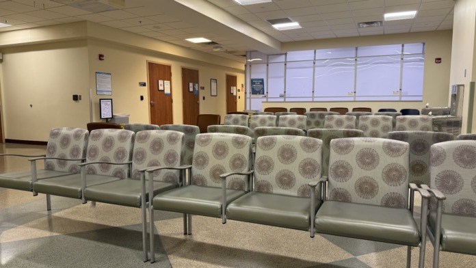 Interior community lounge with multiple upholstered chairs with patterned fabric, windows with natural light, and treatment area seating