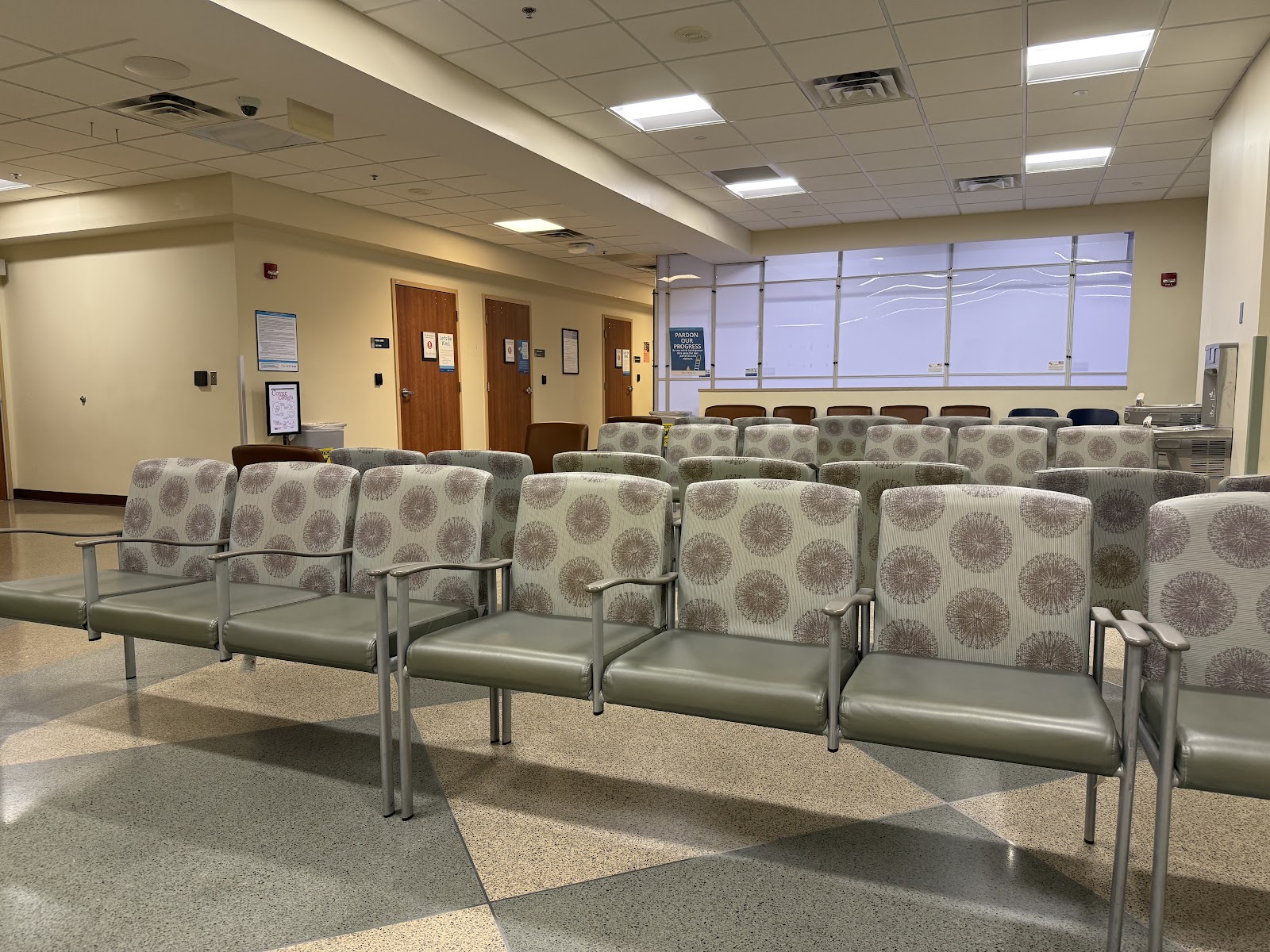 Interior community lounge with multiple upholstered chairs with patterned fabric, windows with natural light, and treatment area seating